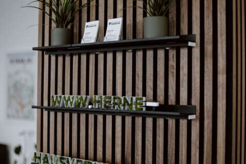 Drei Wandregale mit Pflanzen, Visitenkarten und der Internetadresse www.herne-hausverwaltung.de als begrünte Buchstaben.