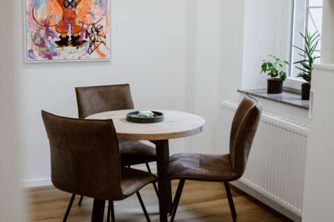 Kleiner, runder Tisch mit drei Stühlen und einem Bild an der Wand.