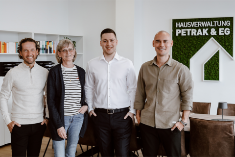 Pascal Groß, Margret Giese, Laurin Petrak und Christopher Eisele im Besprechungszimmer vor dem großen Tisch und dem Firmenlogo in grün an der Wand.