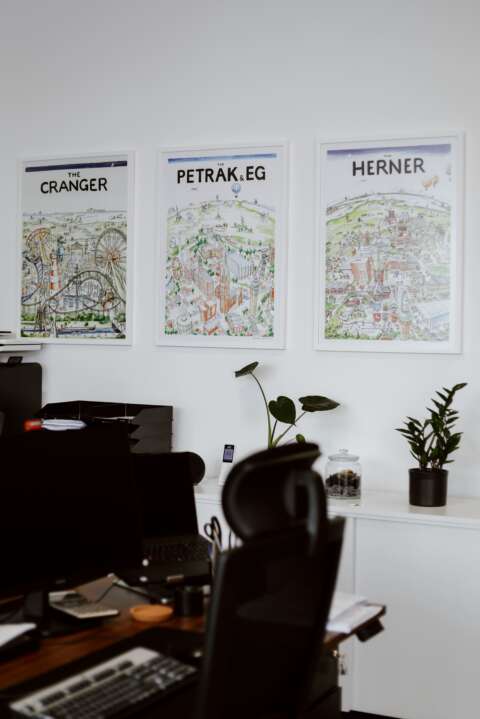 Ein ausgestatteter Arbeitsplatz mit Bildschirm und Bürostuhl, an der Wand drei Bilder von Herne.